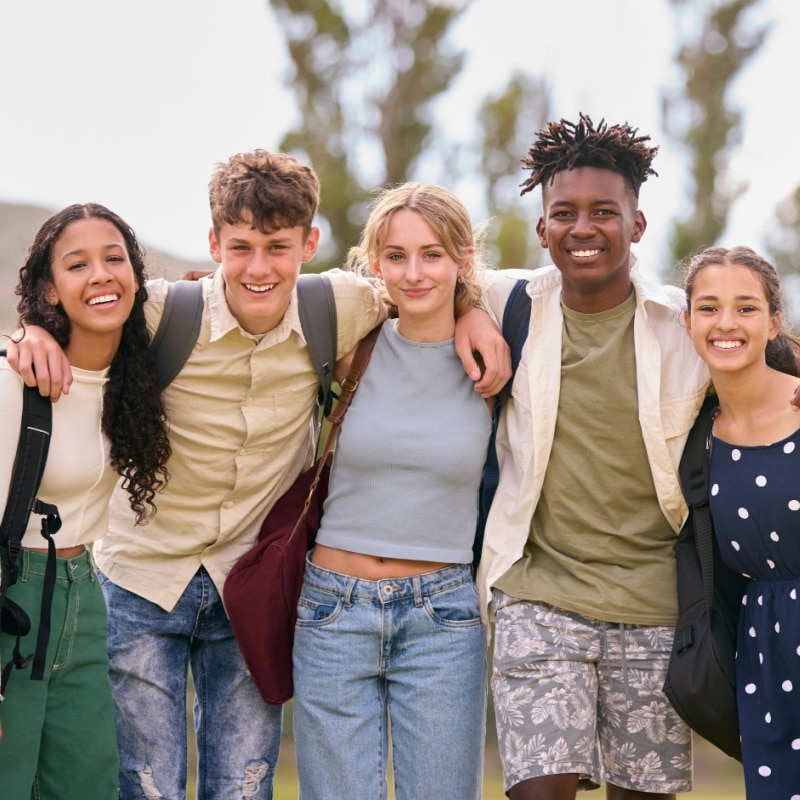 Five smiling teenagers standing arm in arm outdoors