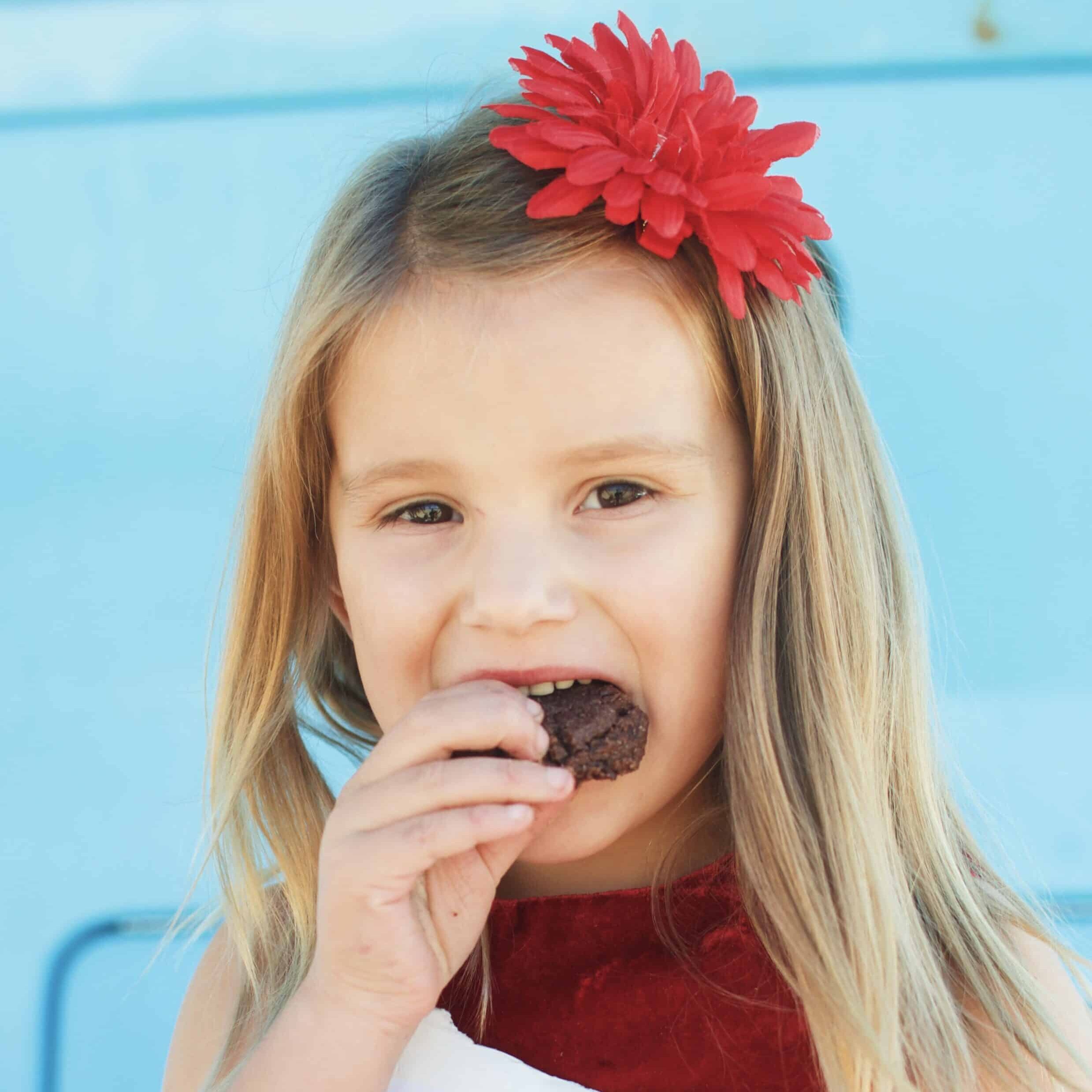 Young girl with a red flower in her hair biting into a chocolate treat