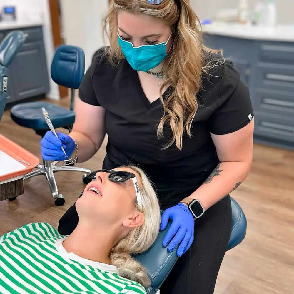 Team member in a mask treating a patient who is wearing sunglasses in the dental chair